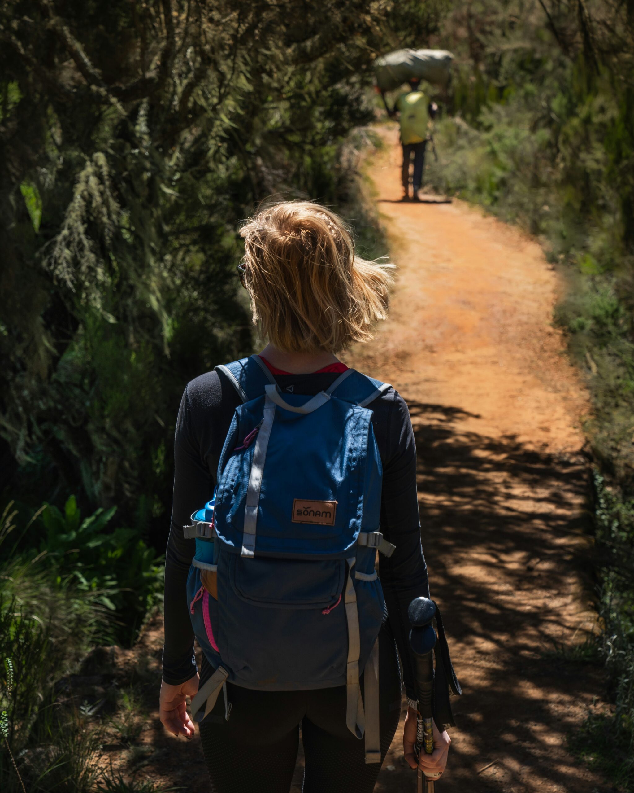 woman in black long sleeve shirt and blue backpack walking on dirt road during daytime